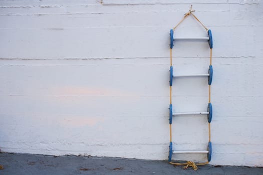 Conceptional geometrical composition of blue marine ladder leaning against vertical white painted wall