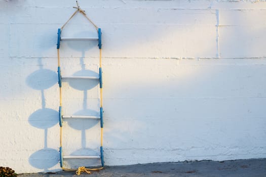 Conceptional geometrical composition of blue marine ladder leaning against vertical white painted wall with sunny shadows