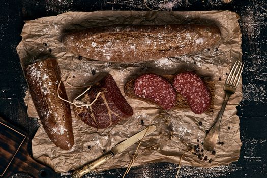 Raw smoked sausage with rye bread on parchment paper with elements of kitchen utensils