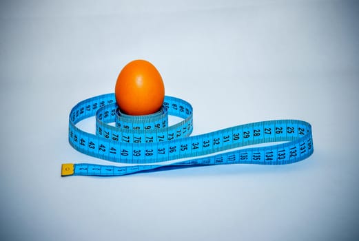 Egg wrapped in blue measuring tape, slimming concept.