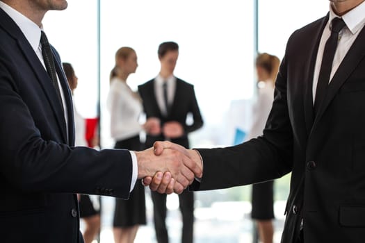 Business handshake at meeting, team of people on background