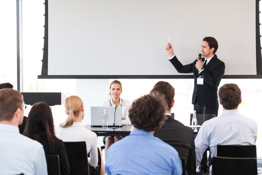 Speaker at business conference near white screen and audience