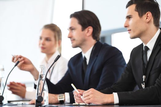 Group of speakers at business meeting at the table with microphones