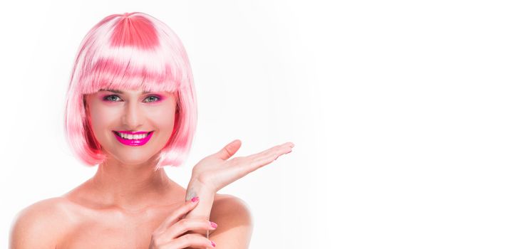 Girl in pink wig with colorful make-up pointing with hand at white copy space