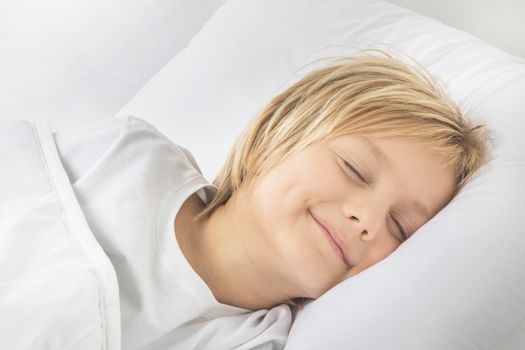 Cheerful smiling blond boy sleep in white bed