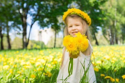 Little girl with a wreath od flowers on head, giving you bouquet of dandelions