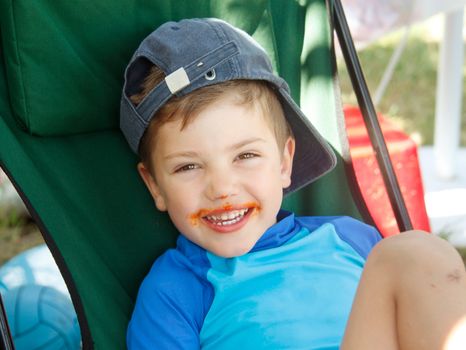 Portrait of a smiling little boy with red sauce around his mouth.