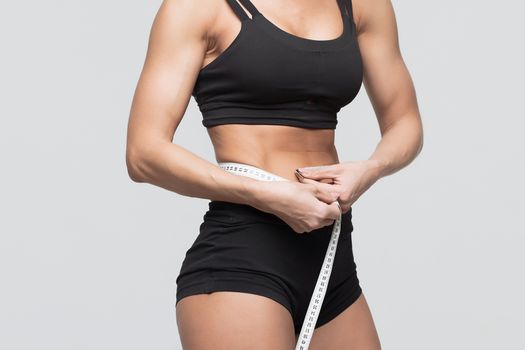 Bodybuilder girl measures the waist measuring tape on a gray background