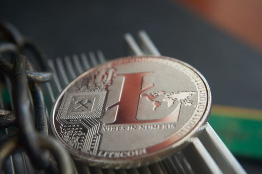 Silver litecoin coin  lying on the  aluminum computer cooler next to a copper chain. Cryptocurrency digging difficulty, blockchain and network concept, selective focus.