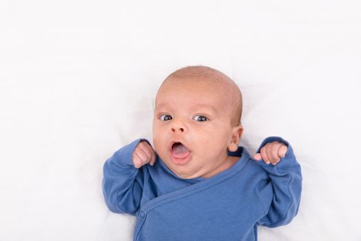 Cute eurasian newborn baby boy wearing a blue infant bodysuit on white sheet and looking at the camera, with copy space