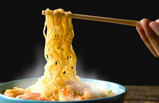Hand using chopsticks pickup instant noodles with smokes isolated on black background.