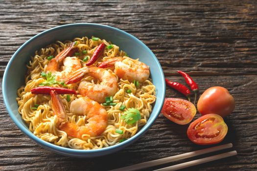 Top view of instant noodles with shrimp and chopsticks on wooden background.
