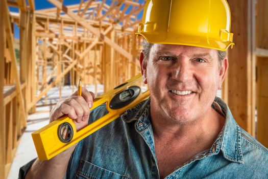 Smiling Contractor in Hard Hat Holding Level and Pencil At Construction Site.