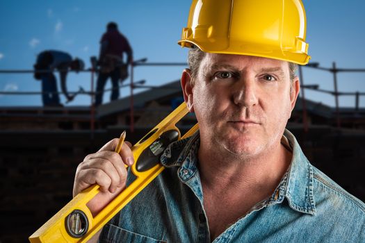 Serious Contractor in Hard Hat Holding Level and Pencil At Construction Site.