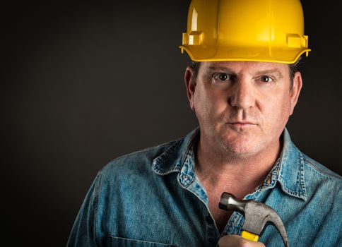 Serious Contractor in Hard Hat Holding Hammer With Dramatic Lighting.