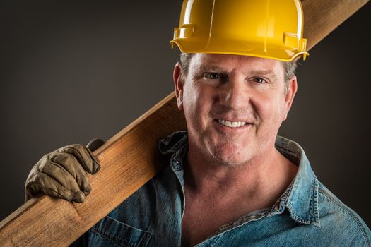 Smiling Contractor in Hard Hat Holding Plank of Wood With Dramatic Lighting.