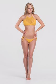 Blonde girl in swimsuit on grey background. Beautiful and healthy woman posing over grey background.