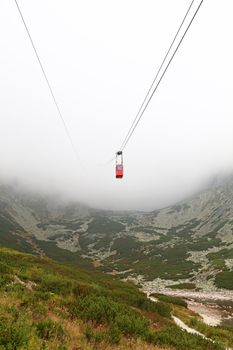 Red mountain cableway car lift in clouds and fog, low angle view