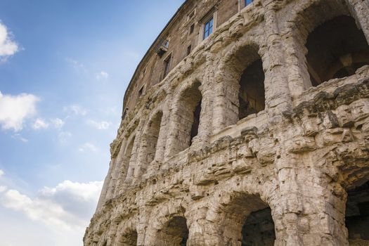 Scenic view on the ancient Theatre of Marcellus (Teatro di Marcello) and ruin of old building (antique columns and detail of the cornice) next to it on the background of clouds.Rome. Italy. Europe.