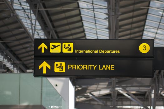 Departure and priority lane information board sign with yellow and white character on black background at international airport terminal.