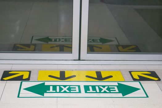 Direction arrows and exit arrow sign at floor of station platform with close door. People will wait for commuting at subway electric train station.