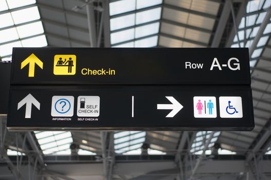 Self check-in and toilets information board sign with yellow and white character on black background at international airport terminal.