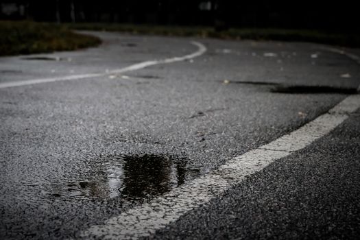 Asphalt track at an old school stadium during a rain with a puddle in the foreground. Dark autumn day