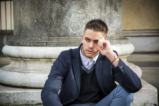Handsome young man outdoor wearing jacket and shirt sitting by historic building in European city. Turin, Italy