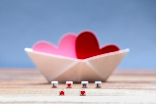 Paper hearts inside paper boat with blue background and incorrect love word
