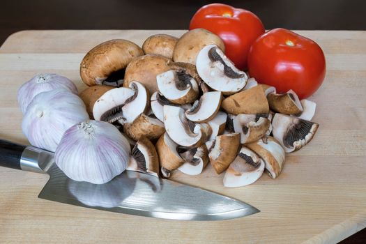 Portobello mushrooms tomatoes garlic cloves vegetable with kitchen knife on wood cutting board closeup