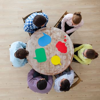 Team of business people in casual clothes sitting around the table with paper dialog boxes, discussing opinion concept