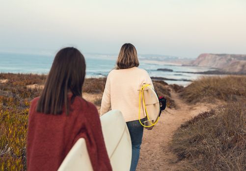 Two female surfers walking near the coastline with surfboards