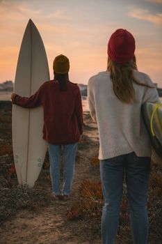 Shot of two female friends holding their surfboards while looking to the ocean