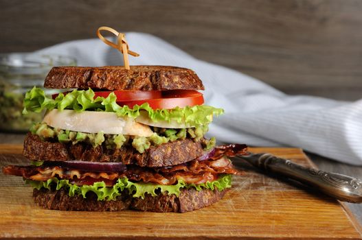 A double sandwich made of Greek bread with slices of fried bacon, avocado, boiled chicken breast, and tomatoes.