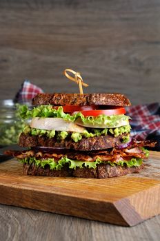 A double sandwich made of Greek bread with slices of fried bacon, avocado, boiled chicken breast, and tomatoes.