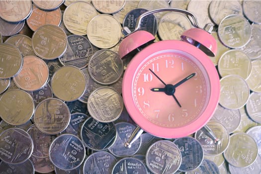 Stack of coins with pink fashioned alarm clock for display planning money financial and business accounting concept, time is money concept with clock and coins, time to work at make money, vintage color tone
