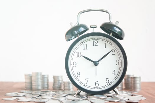 Stack of coins with black fashioned alarm clock for display planning money financial and business accounting concept, time is money concept with clock and coins, time to work at make money, vintage color tone