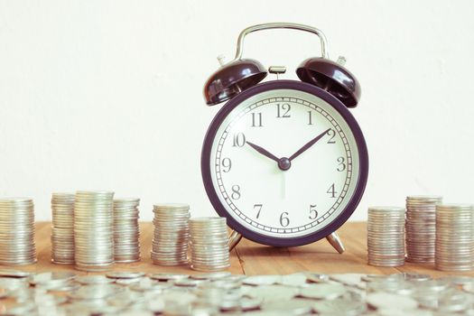 Stack of coins with black fashioned alarm clock for display planning money financial and business accounting concept, time is money concept with clock and coins, time to work at make money, vintage color tone