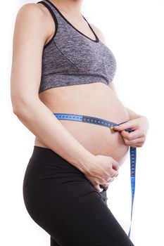 Pregnant woman measures her belly with a measure.