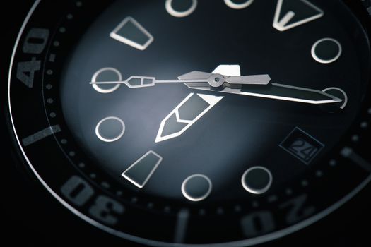 Low key of macro on moving of black classic automatic watch with silver clock hands around six o’clock. Glass of watch reflecting white light.