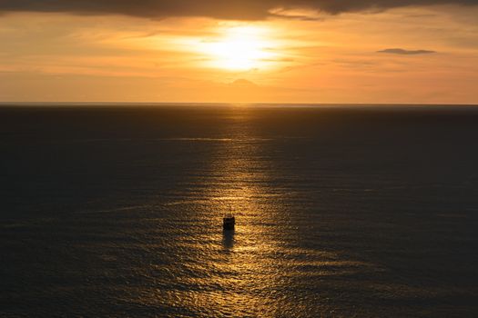 Old ancient ship on peaceful ocean at sunset. Calm waves reflection, sun setting.