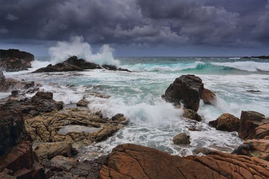 Stormy skies over rugged coastline with waves crashing over rocks.  Australia