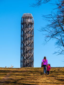 Young woman with doughter walks toward wooden lookout tower in Hermanice, Czech Republic.