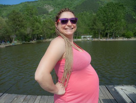 Happy pregnant woman with pink singlet, small dam in the background.