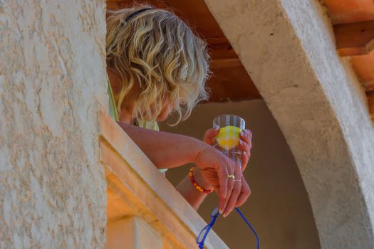 Woman relaxing on a Mediterranean balcony. In the hand a glass of water with lemon slices.