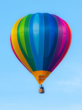 Hot air balloon in rainbow spectrum colors on blue sky background.