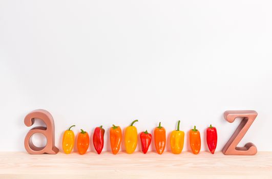 Sweet peppers A to Z. Row of colorful paprika on wooden surface.