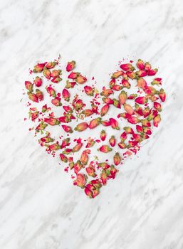 Heart made of dried rose flowers, on light gray marble background.