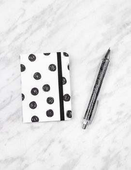 Little black and white diary and pen on marble background.