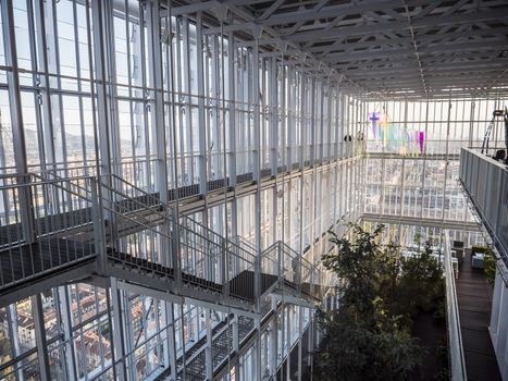 From above shot of huge glass interior building with stairs and levels and green trees growing below.